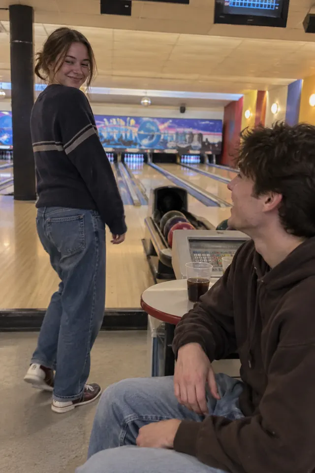 Two students at a bowling alley, one turning back with a grin